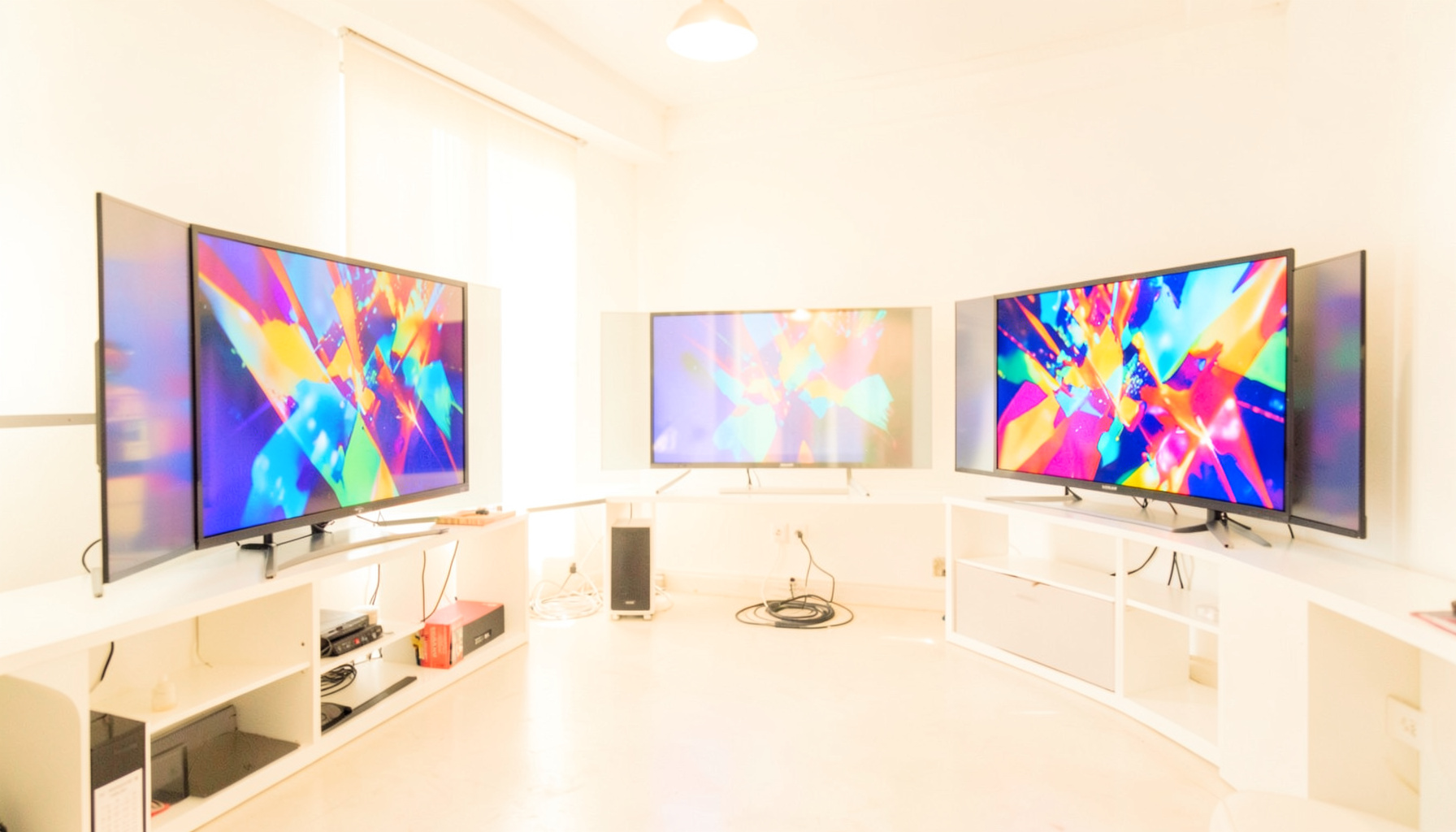 A bright, airy studio space with television monitors displaying abstract colorful patterns, warm ambient light filling the room